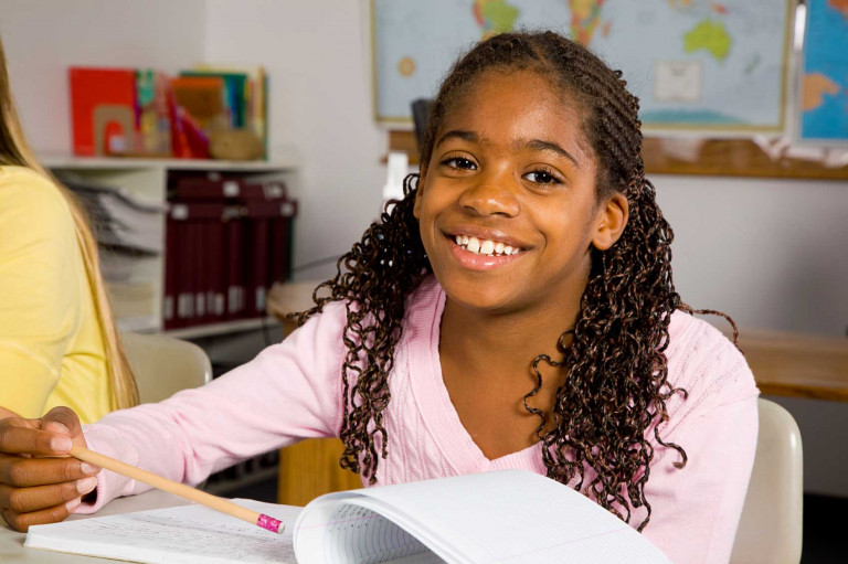 Young-student-at-desk-with-book-smiling-at-camera-1698x1131