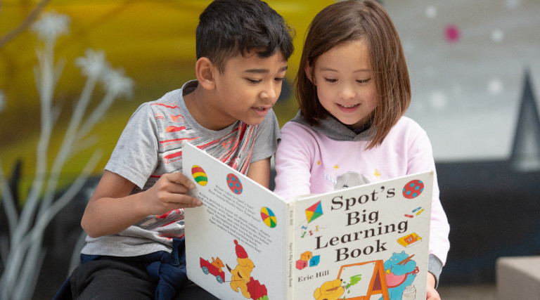 Close-up of elementary boy and girl reading on bench